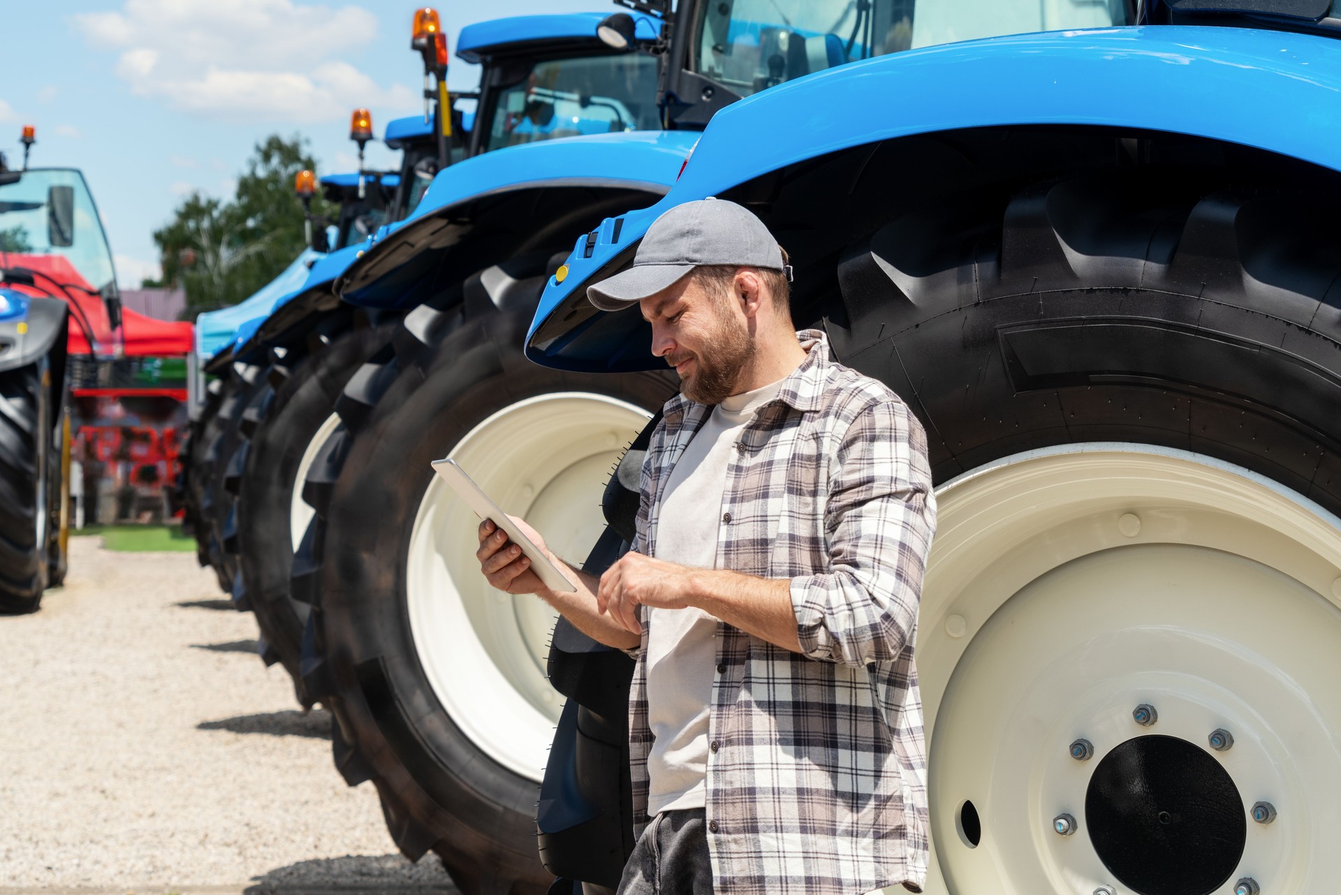 Man farmer stands next to new farm tractors at agricultural machinery dealership and using digital tablet.